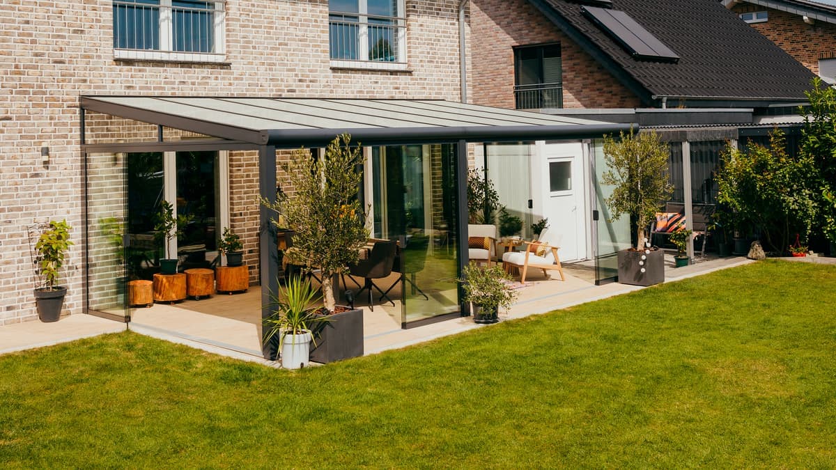 Véranda avec parois coulissantes en verre et éclairage d'ambiance Terrasoverkapping aan een woning bij zonsondergang, met een stel dat ontspannen op een comfortabele bank zit.Véranda avec parois coulissantes en verre et éclairage d'ambiance
